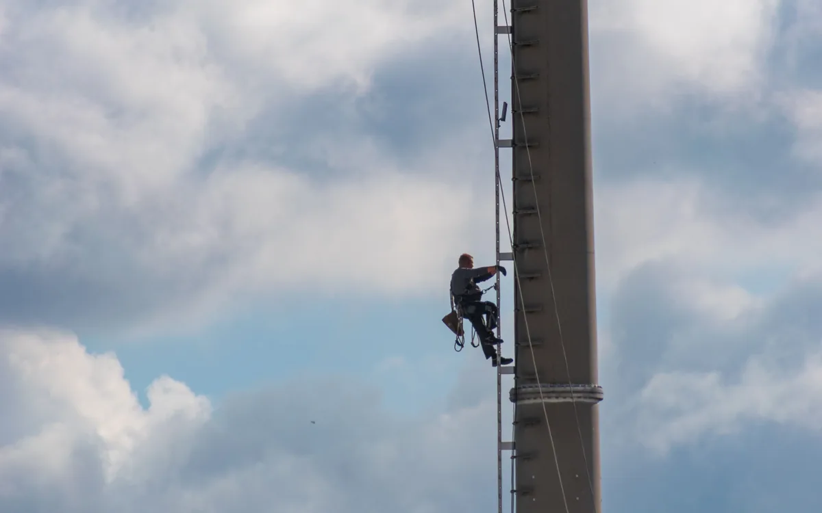 Safety-equipped telecom tower climber ascending a steel lattice structure